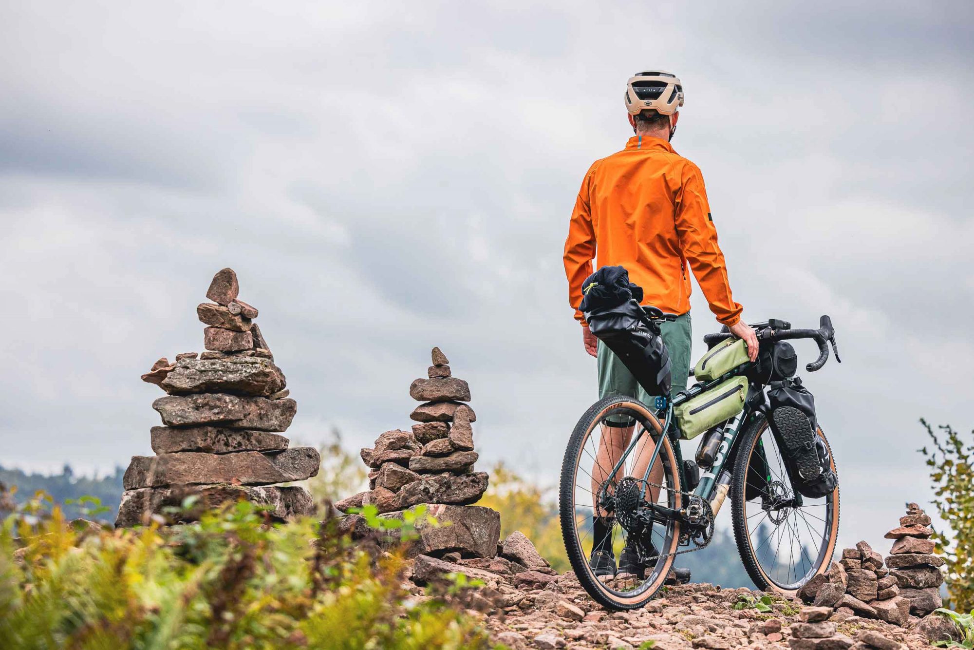 Ein Gravelbiker steht auf einem Hügel und schaut in die Ferne