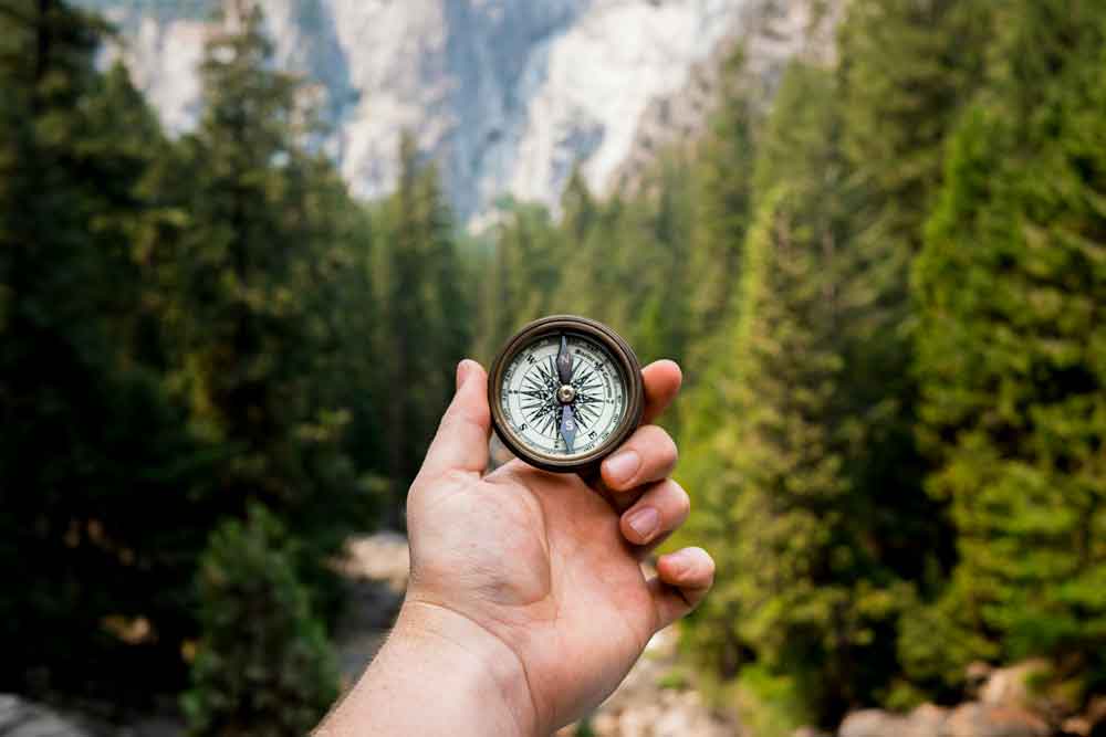 Eine person hält einen kompass in die höhe, im hintergrund eine schöne berglandschaft. Dieses bild symbolisiert die seite leitbild. Foto von foto von jamie street/unsplash