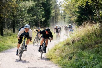 Eine gruppe von gravelbikern fährt rasant einen abschüssigen schotterweg hinab und hat offenbar viel spaß dabei.