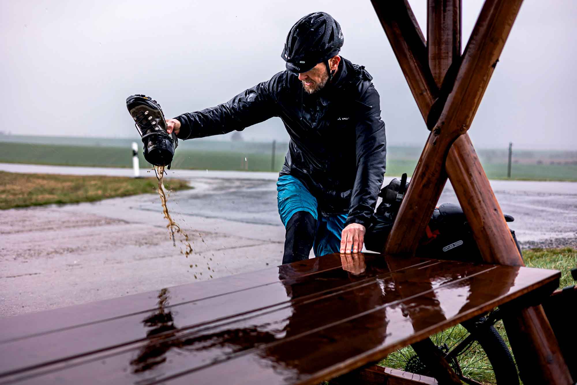 Ein radfahrer ist in den regen gekommen und macht eine pause, um seinen völlig durchnässten schuh „auszuschütten“.