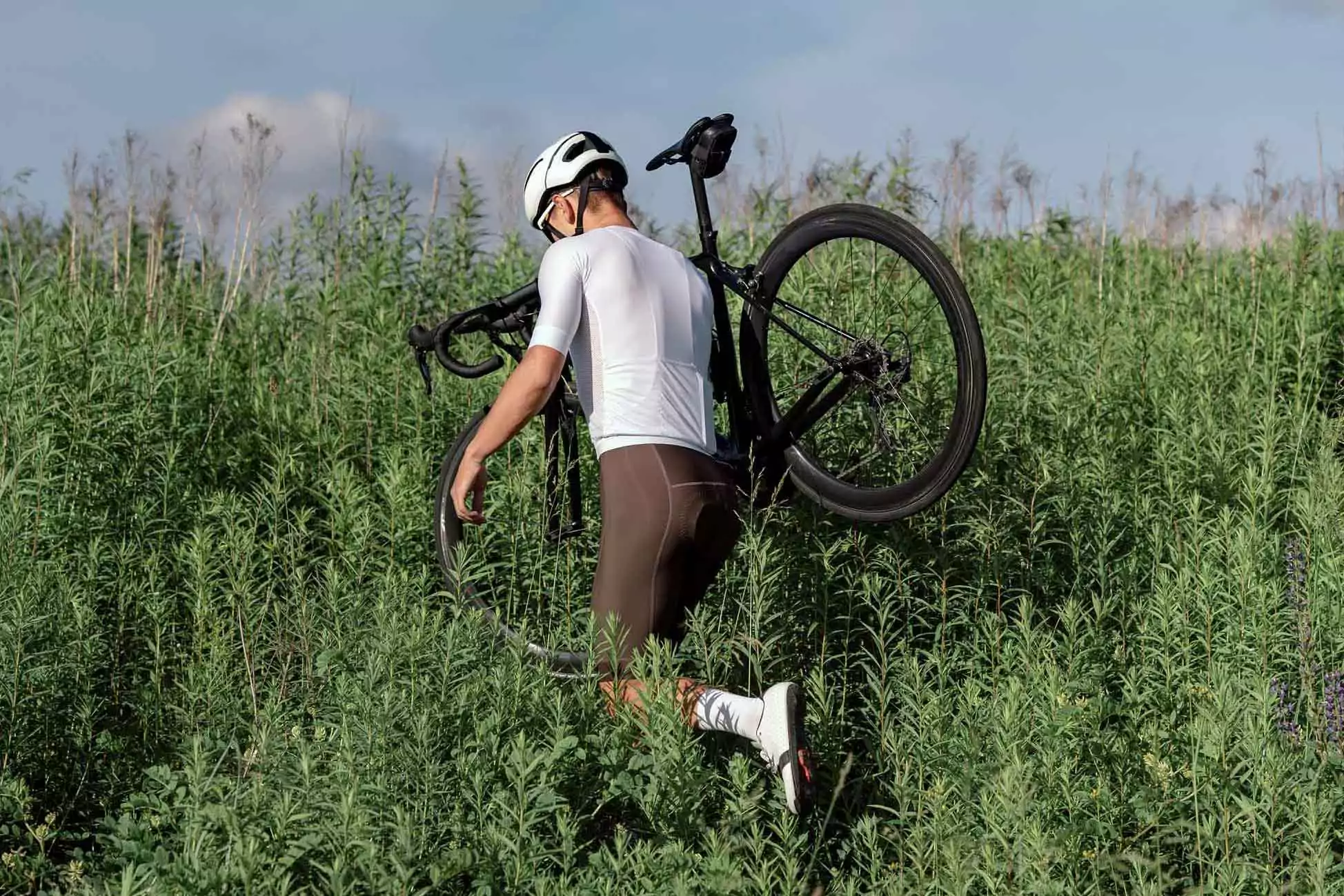 Sportler_im_feld Ein rennradfahrer schultert sein rennrad und stapft durch ein feld. Das soll symbolisieren, dass jobrad loop für alle wege das passende fahrrad hat.